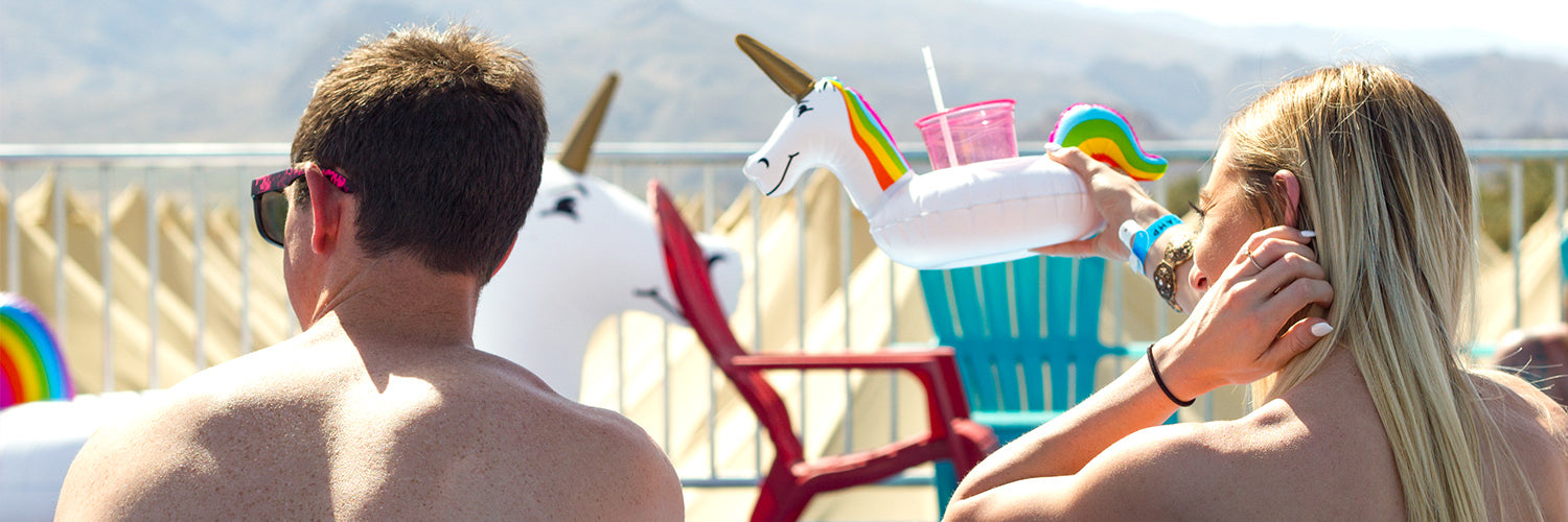 Two people relaxing with unicorn drink holders outdoors, mountains in the background.