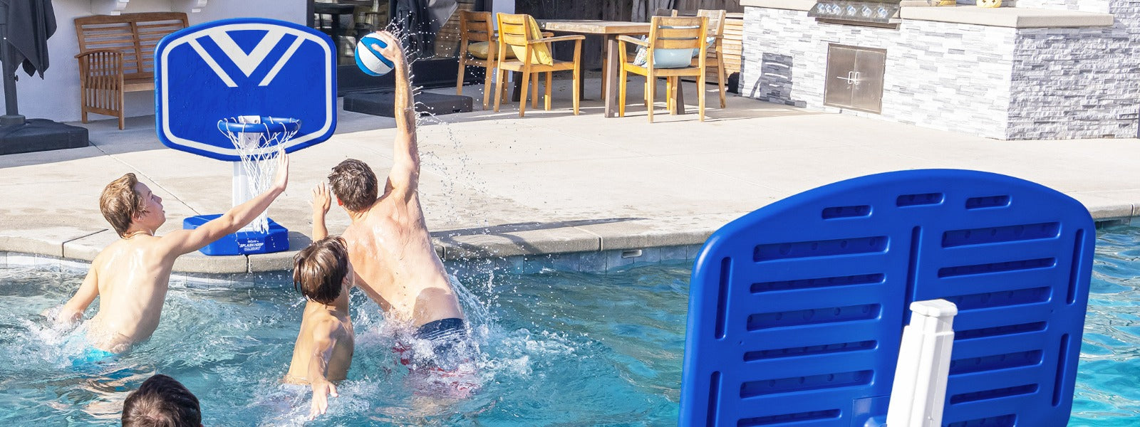 Three people playing basketball in a swimming pool with blue and white poolside basketball hoops.